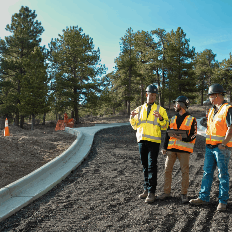 Three construction workers in safety gear discuss plans on site.