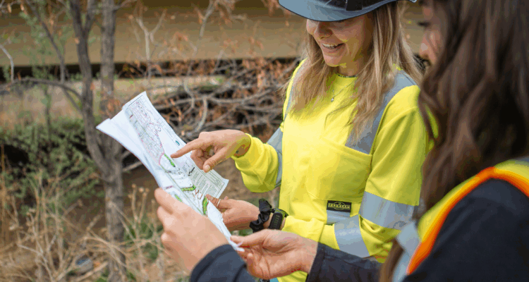 Two people in safety gear review construction project plans outdoors.