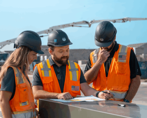 Three construction workers review plans at a construction site.