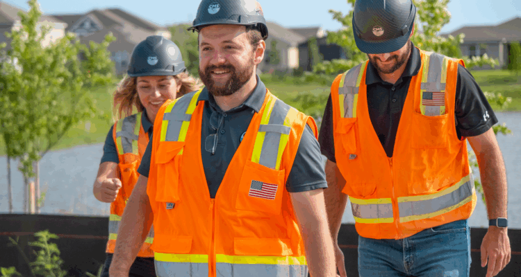 Three people in orange safety vests walk at construction site.