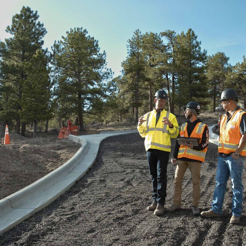 Three construction workers in safety gear discuss plans on site.