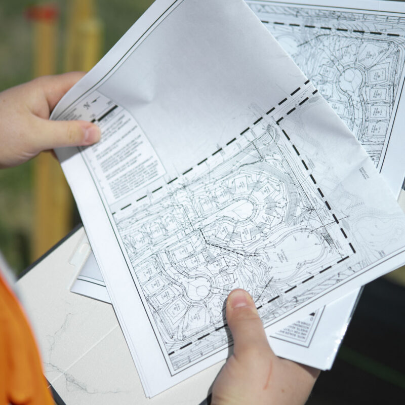 Person in orange jacket reviews construction project plans outdoors.