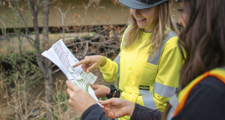 Two people in safety gear review construction project plans outdoors.