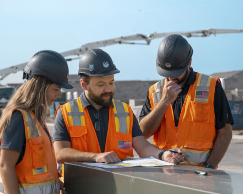 Three construction workers review plans at a construction site.