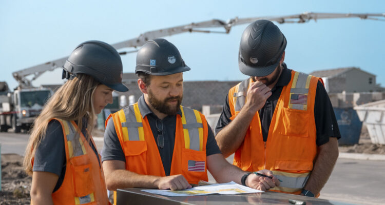 Three construction workers review plans at a construction site.
